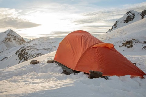 An orange tent nestled in a serene snowy mountain setting, perfect for ski touring. The peaceful