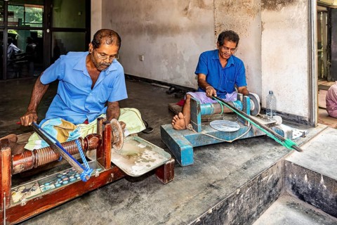 Two men in blue work clothes work on machines in parallel, the gemstone cutters in the city of