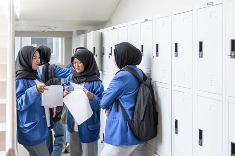 Asian Muslim students gather at lockers, discussing schoolwork as they prepare to return to school.