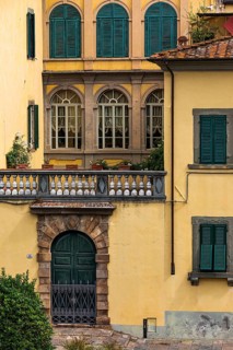 Arched entrance gate and arched windows with green shutters in a pastel-coloured façade, historic