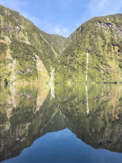 Mountains with reflections in the water against a blue sky in Doubtful Sound, South Island, New