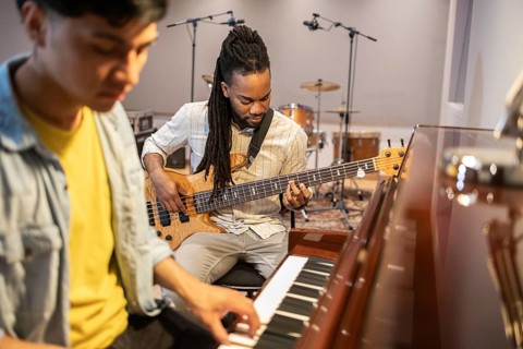Musicians are collaborating passionately in a recording studio. One plays the piano while the other