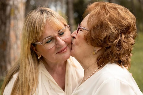 An elderly mother lovingly kisses her adult daughter on the cheek, showcasing the warmth and