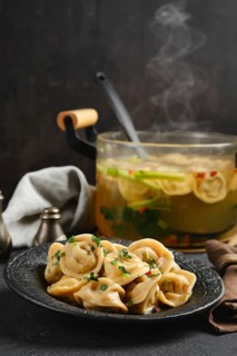 A plate of freshly made dumplings garnished with herbs is placed beside a steaming pot of broth