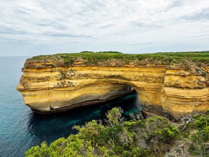 A stunning coastal rock formation forming a natural arch over azure waters, surrounded by lush