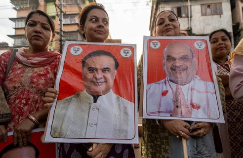 Supporters hold placards featuring Amit Shah and Himanta Bishwa Sarma during a public rally of the