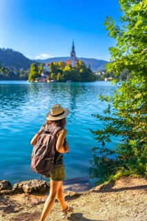 Female tourist walking along the shore of lake bled in slovenia, admiring the pilgrimage church of