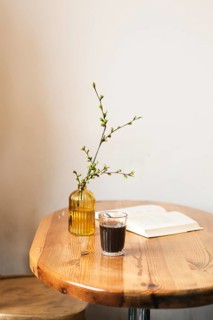 A cozy scene featuring a glass of coffee, an open book, and a vase with blooming branches on a