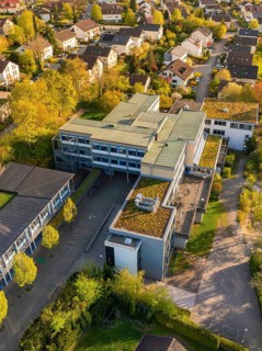 Aerial view of a modern building surrounded by trees in autumnal colours in a residential area,