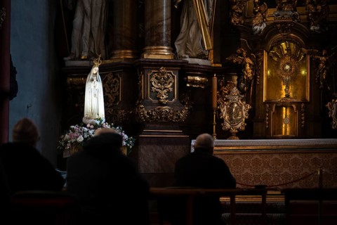 Devout people praying in a dim baroque church before the Blessed Sacrament and a statue of the