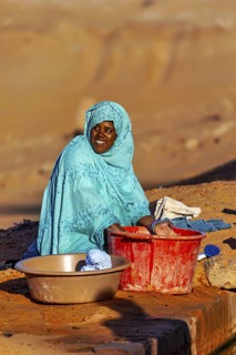 Smiling woman in traditional dress working with bowls in a desert environment, woman washing
