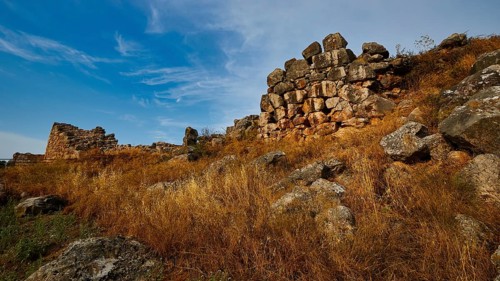 Old stone ruins on a hill with dry grass and blue sky, Tiryns, ancient city in Argolis, Mycenaean,
