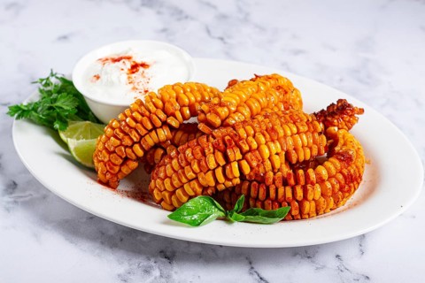 Corn ribs, with cream sauce, spices and lime, appetizer, on a white plate, homemade, no people