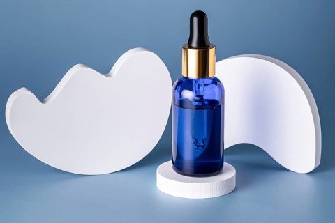 Elegant blue glass bottle with a dropper on a geometric white podium against a blue background