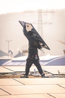 Worker handling a solar panel on a roof, sunlight and urban environment, PV installation at OBI