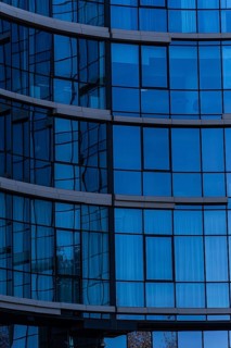 A close-up view of a modern office building, showcasing a curved glass facade with visible metal