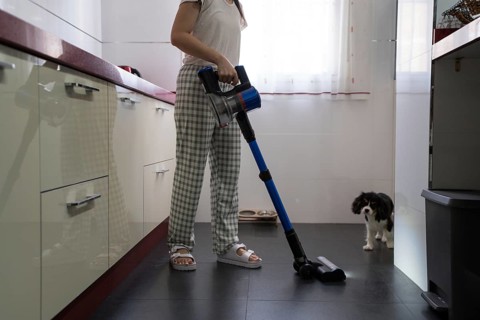 Woman uses a cordless vacuum cleaner in a bright kitchen, maintaining cleanliness and hygiene. A