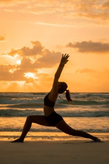 A silhouette of a woman performing yoga on the beach as the sun sets, casting a warm glow in Tulum,