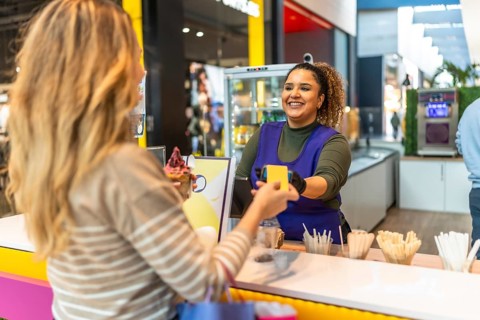 Customer paying with contactless card while smiling cashier completes sweet shop sale at mall