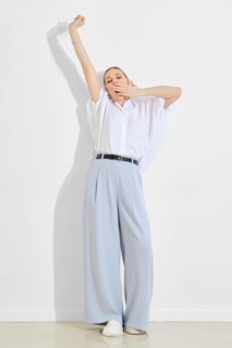A woman in a casual outfit is stretching her arms above her head and yawning while standing against