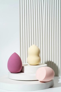 Pastel-colored cosmetic sponges arranged on white geometric platforms against a textured white
