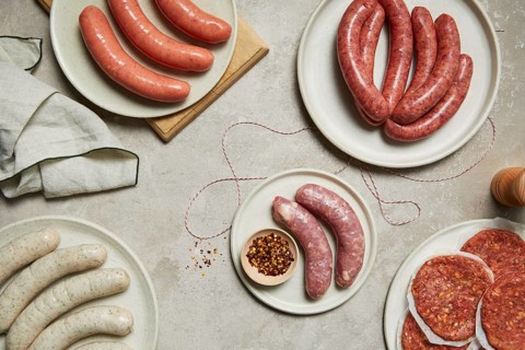 An assortment of sausages and meats displayed on white plates, showcasing a variety of textures and