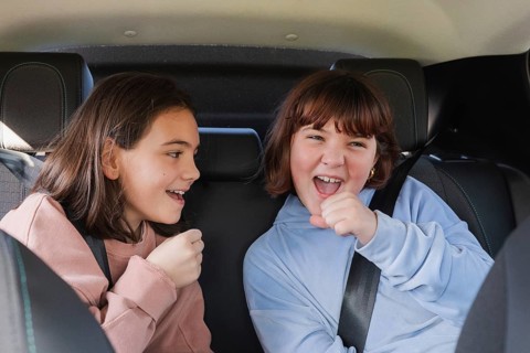 Two young girls wearing seatbelts enjoy a fun moment in the backseat of an electric car, singing