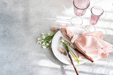 Top view of a stylish table setting featuring fresh snowdrops, a white ceramic plate, pink cloth