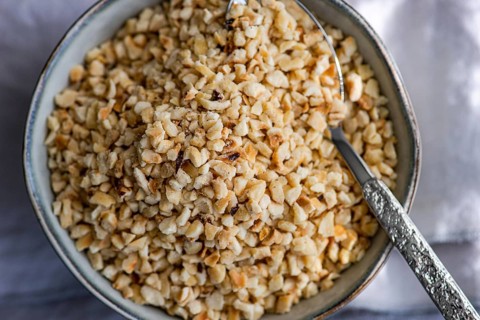 Top view of finely chopped hazelnuts in a rustic bowl with a silver spoon, ideal for baking and