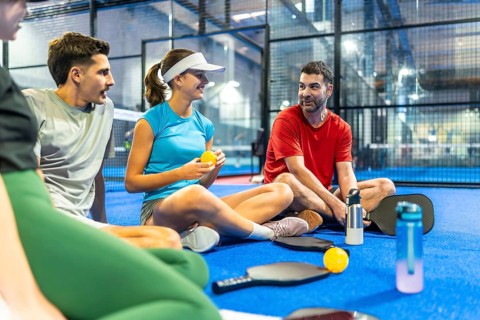 Group of diverse friends relaxing and chatting together on the blue pickleball court surface,