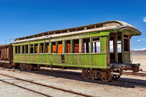 Rusty green passenger car stands alone on rails in a barren desert environment, railroad cars in