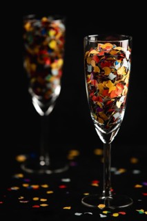 Champagne glasses filled with colourful confetti, confetti scattered on a black background