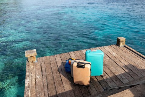 Travel bags on a weathered wooden pier overlooking the crystal-clear waters of Kri Island in the