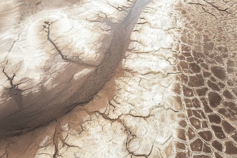 Aerial view capturing the stark textures of a cracked, dry riverbed snaking through an arid and