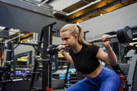 A determined blonde woman performs a squat with a barbell in a spacious, well equipped gym. The