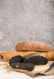 Sliced black bread with different kinds of fresh baked bread on a gray concrete background. side