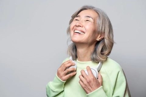 Asian Chinese senior woman smiling joyfully while holding headphones, enjoying her favorite music.