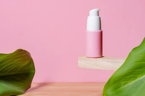 Minimalist presentation of a pink cosmetic skincare dispenser on a wooden shelf, accented with a