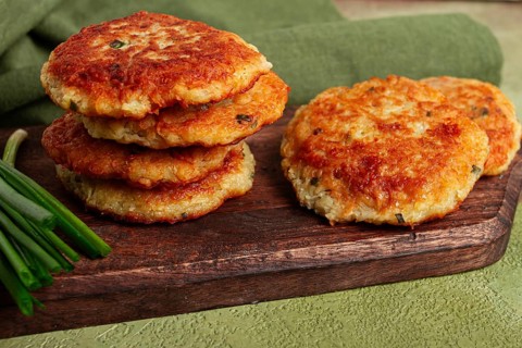 Crispy potato pancakes Latkes, stacked on a wooden board next to fresh green onions, natural light,