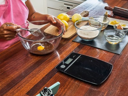 Woman preparing to bake with essential ingredients and tools on a wooden table, including a bowl
