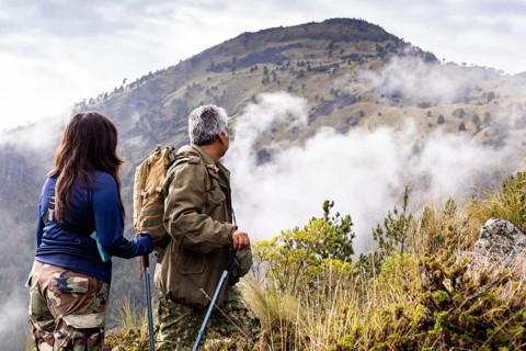 A cheerful pair of hikers enjoys a scenic view of a misty mountain landscape. The adventurers,