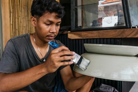 A Balinese artisan meticulously paints a ceramic sculpture, showcasing intricate craftsmanship. The