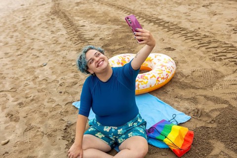 A cheerful transgender man, feeling positive and free, is capturing a selfie moment on a sandy