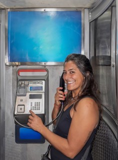 A smiling woman is using a public payphone inside a metallic booth located in Melbourne, Australia.