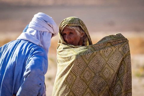 Two people in traditional dress talk in a desert landscape, A Tuareg talks to an old woman in the