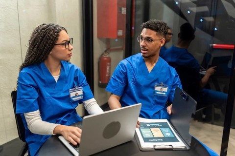 Medical staff in blue scrubs discussing patient information, collaborating on a laptop and