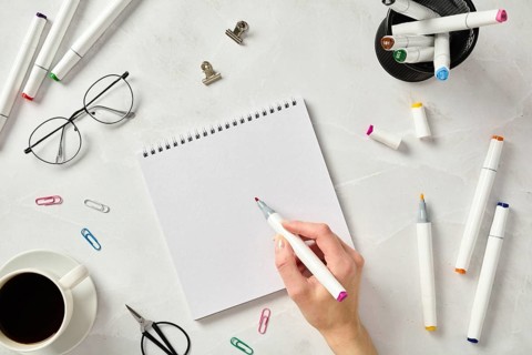 Top view of an artist cropped unrecognizable hand in a workspace features sketching markers, a