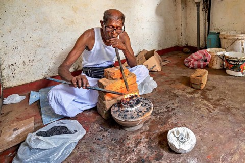 In the workshop, a man blows a pipe into a coal-fired basin, a man burns safire in a small stove in