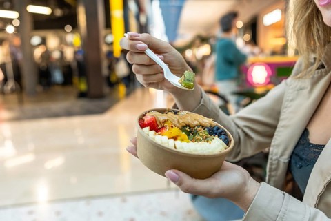 Woman holding biodegradable bowl of colorful acai with kiwi, banana, berries, mango, peanut butter