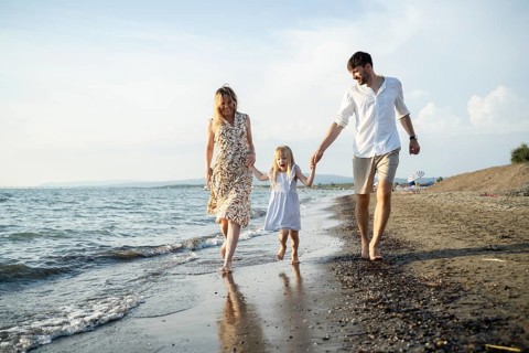 A cheerful family of three enjoys a relaxing walk along the shoreline, holding hands and smiling.
